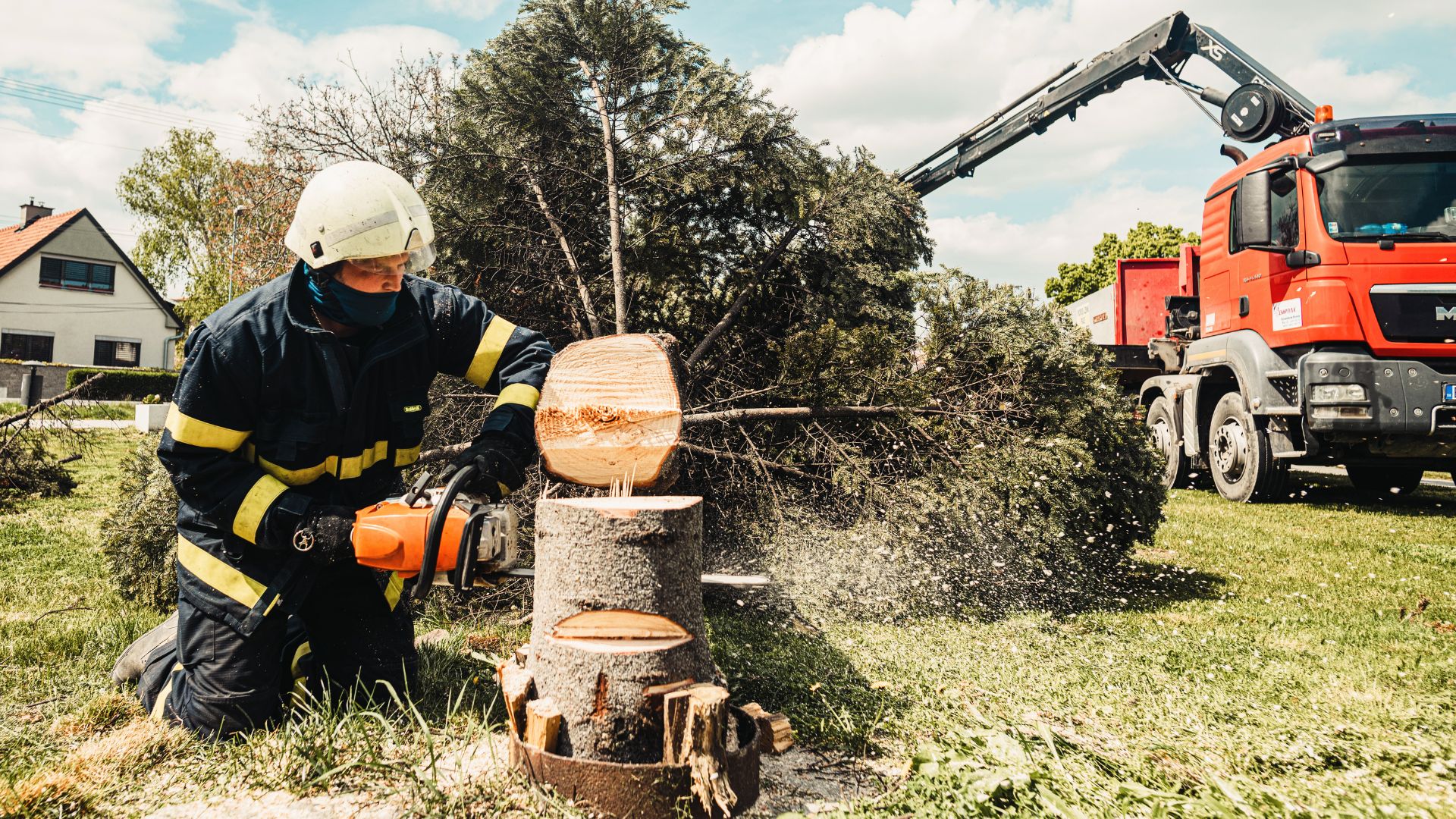 Firefighter cutting tree with chainsaw, red truck in background